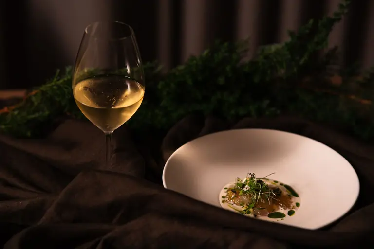A sophisticated gourmet dish paired with white wine, set against a lush background in a Tokyo restaurant.